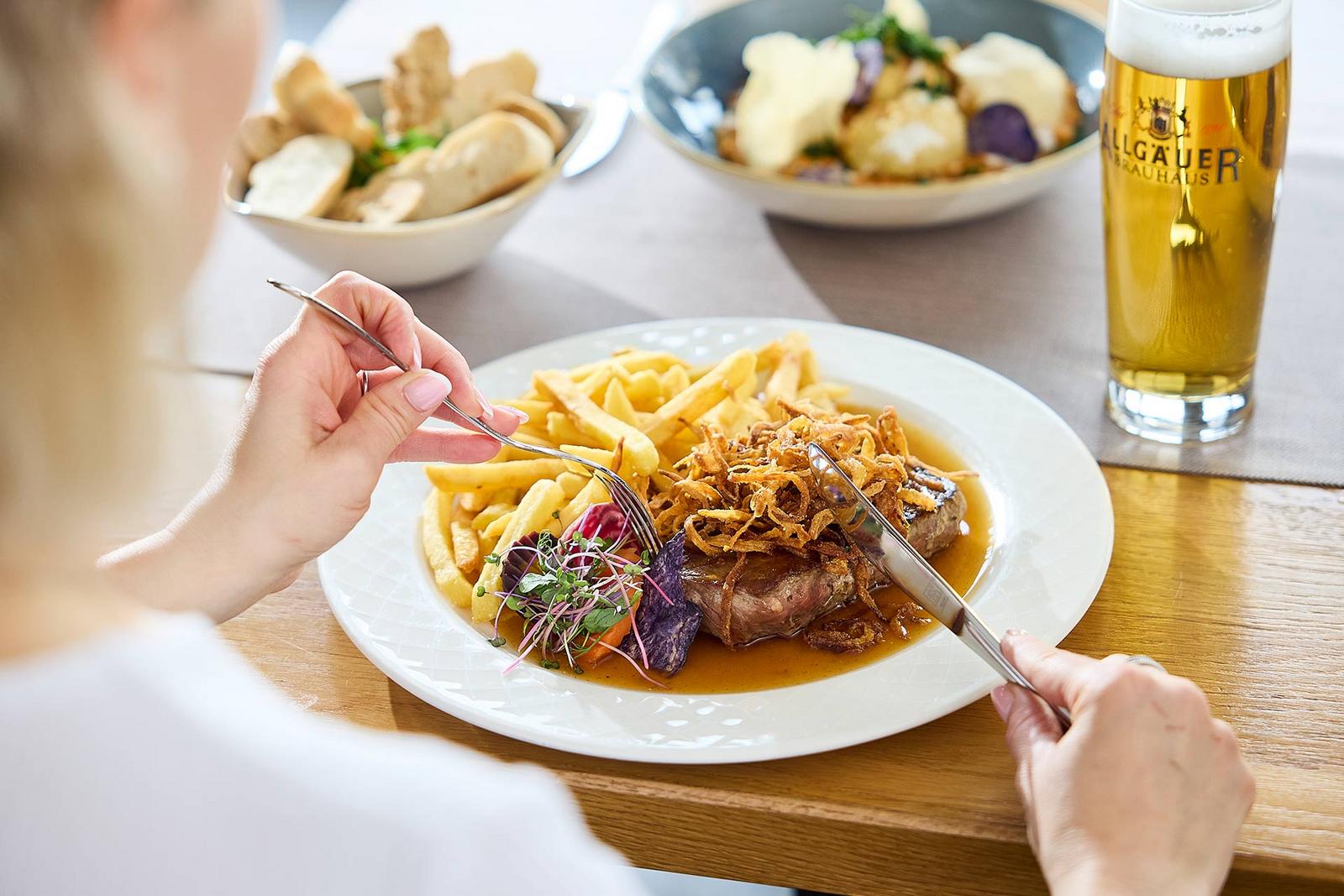 Eine Frau genießt einen saftigen Zwiebelrostbraten mit knusprigen Pommes