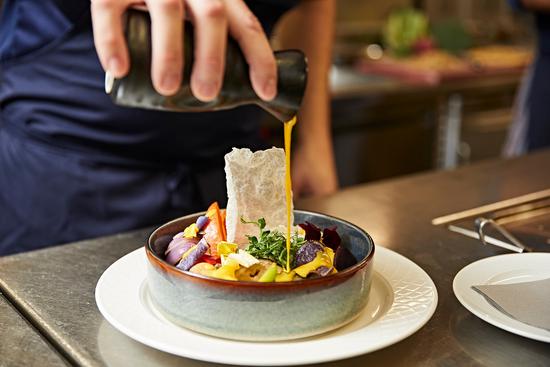 Ein Koch garniert einen Salat mit einem Dressing