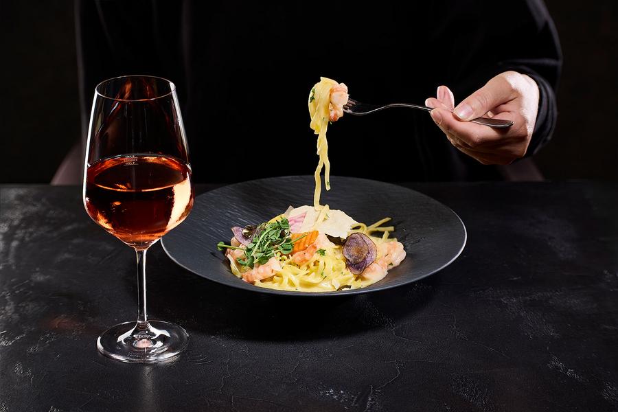 Eine Frau genießt Spagetti mit Garnelen und einem Glas Roséwein