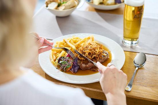 Eine Frau genießt einen saftigen Zwiebelrostbraten mit knusprigen Pommes und frischen Röstzwiebeln