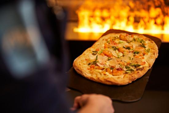 Ein Koch hält einen frischen Flammkuchen vor dem Feuer