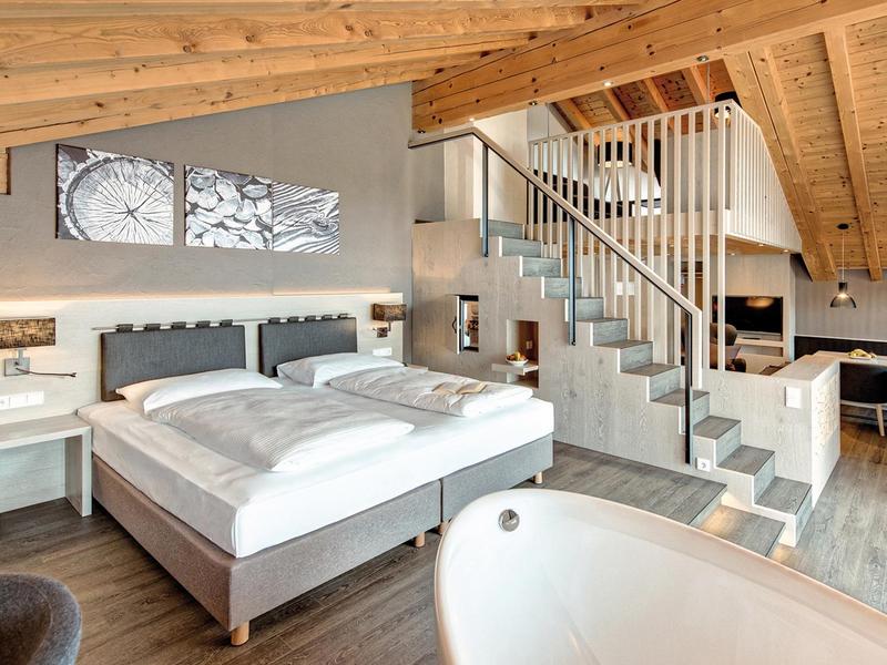 Helle Suite im Hotel Krone: Doppelbett, freistehende Badewanne, Treppe zur Galerie mit Wohnbereich unter sichtbarer Holzbalkendecke.
