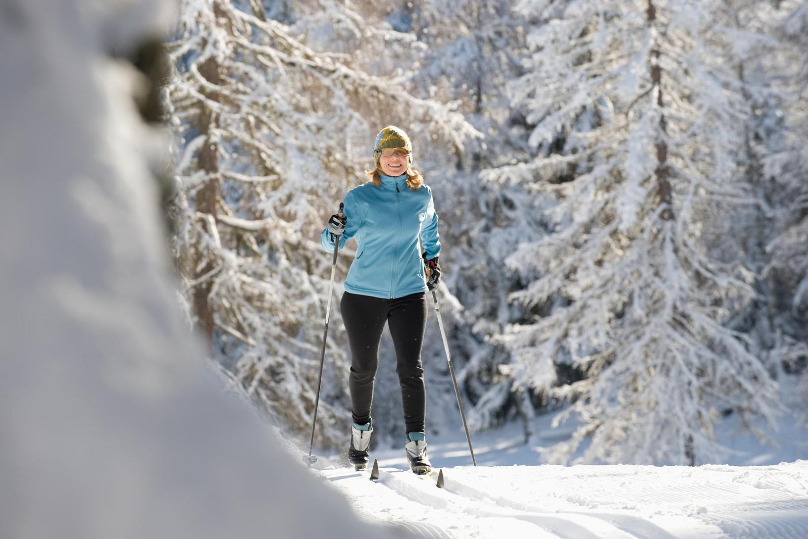 Eine Frau läuft klassisch Langlauf durch einen winterlich verschneiten Wald