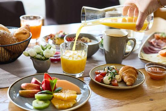 Eine Hand schenkt frischen Orangesaft auf einem üppig gedeckten Frühstückstisch ein