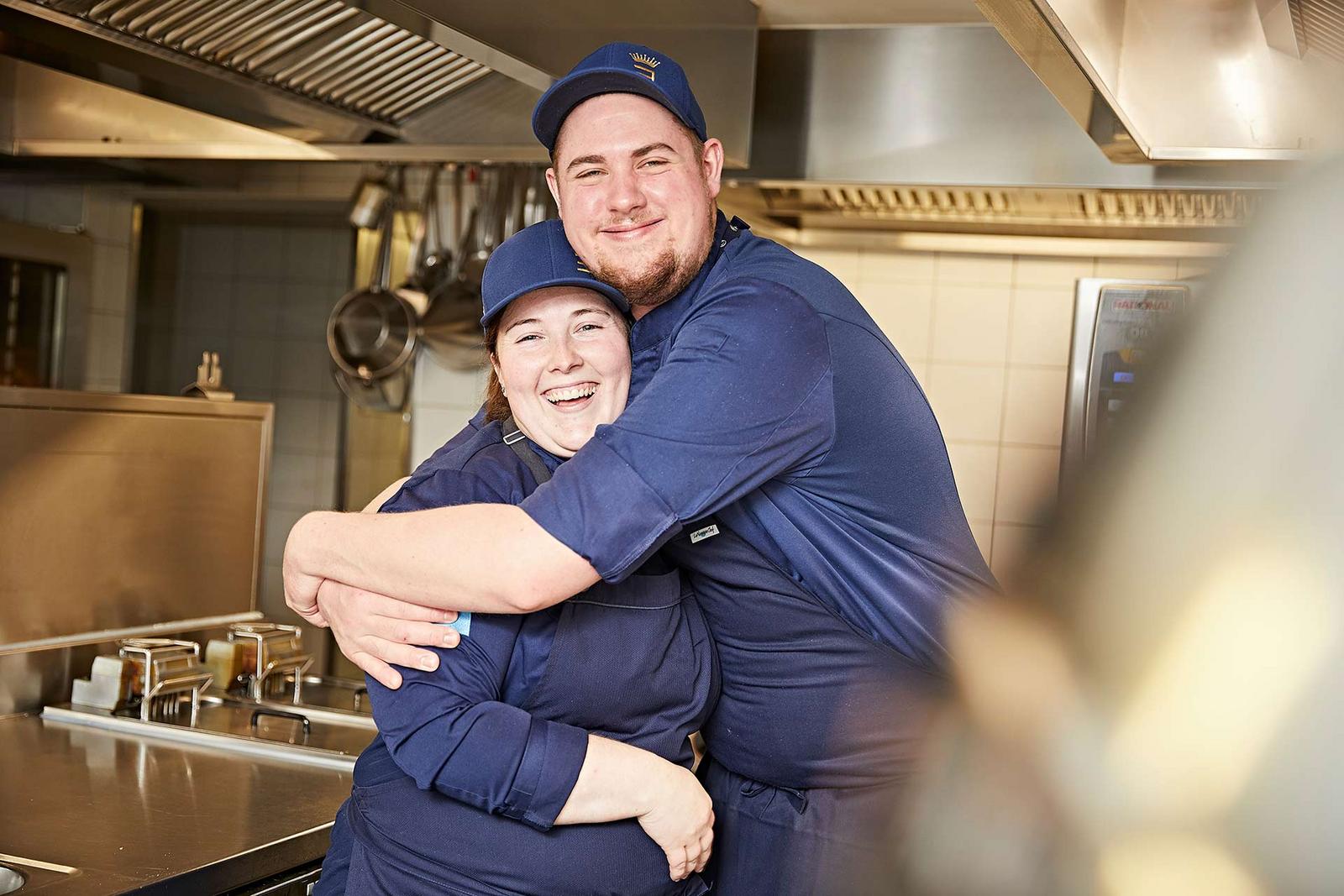 Zwei Köche liegen sich in den Armen und lächeln herzlich in die Kamera