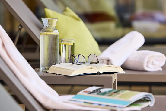 Detailaufnahme einer Sonnenliege mit Buch, Brille und Wasserkaraffe