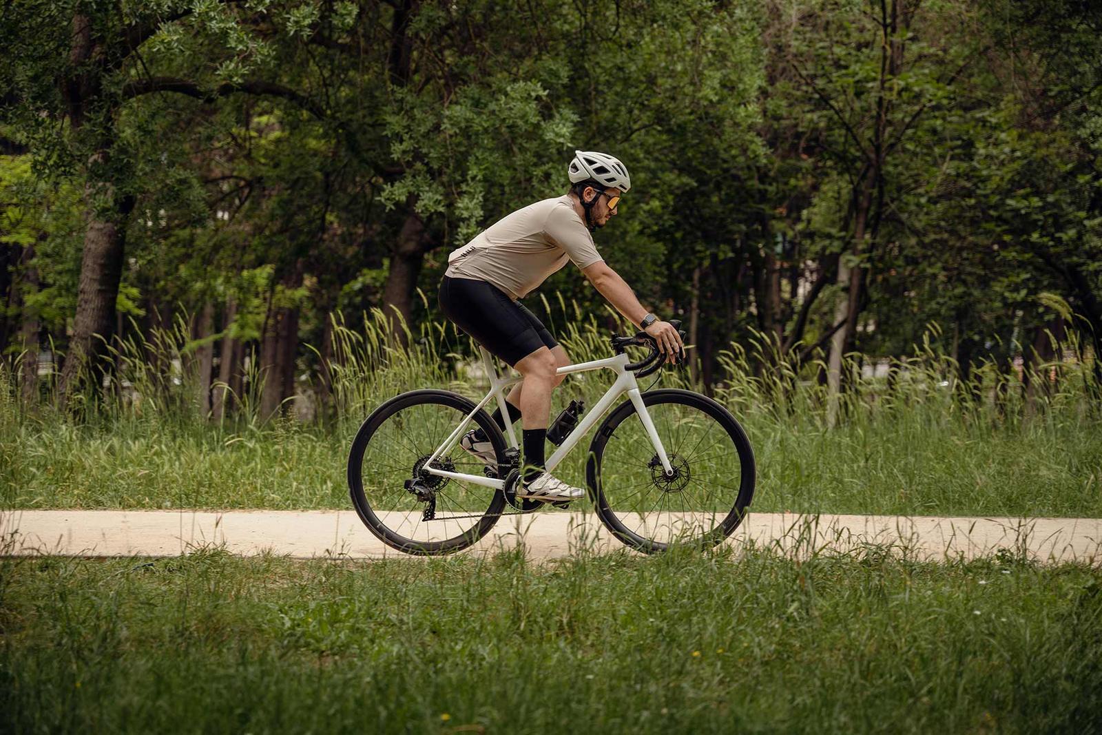 Ein Mann fährt mit einem Gravelbike auf einem Schotterweg durch grüne Wiesen