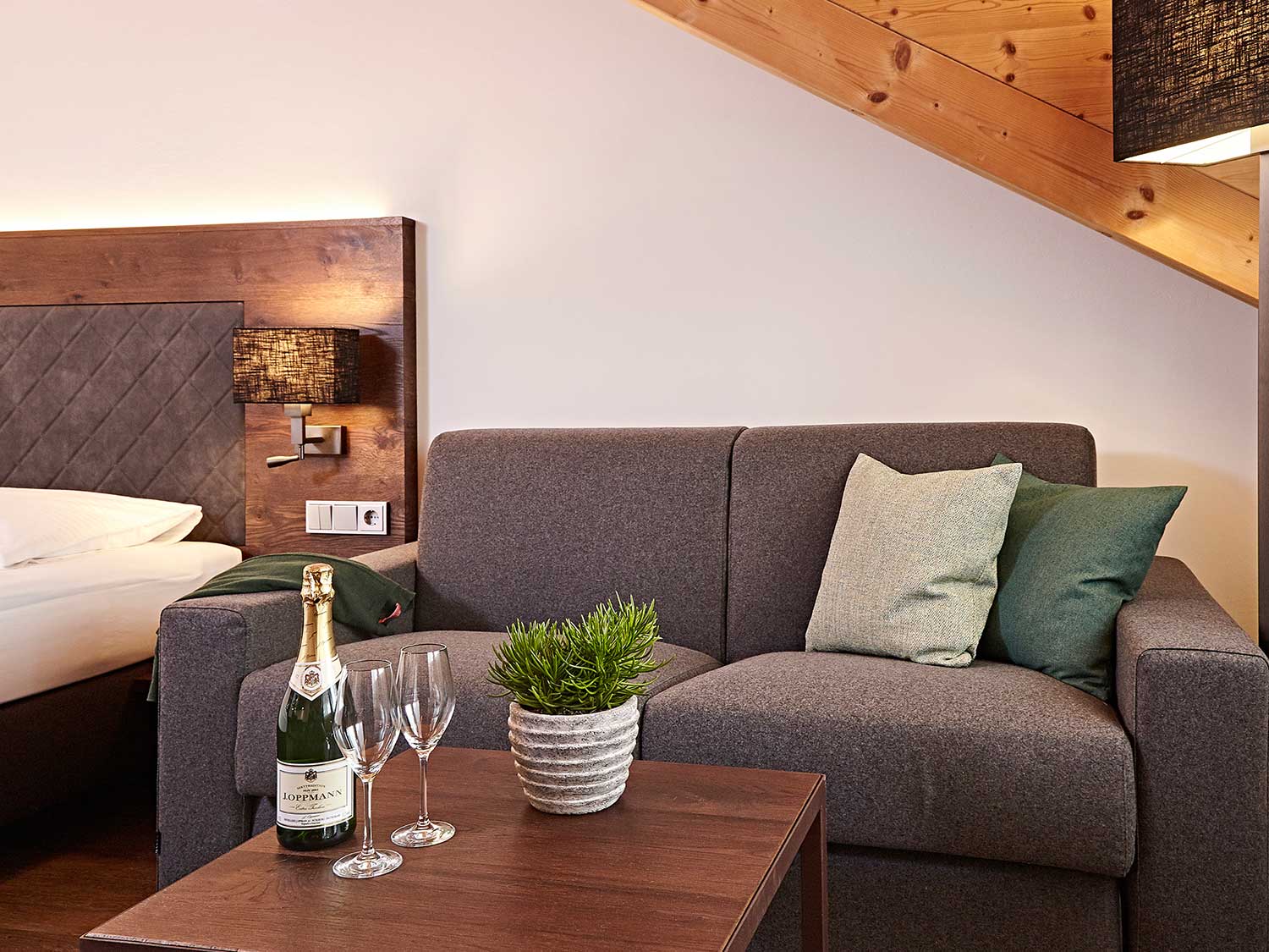 Doppelzimmer Deluxe mit Wohnbereich und graußer Couch und Tisch 