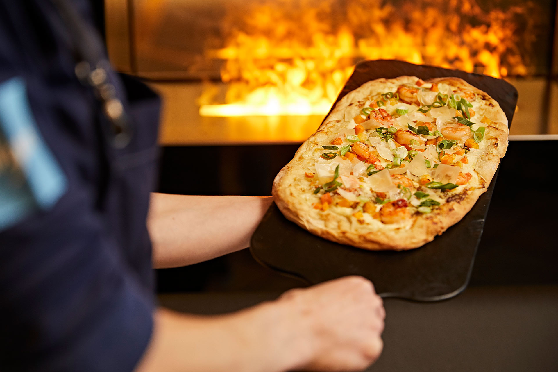 ein Koch hält einen frischen Flammkuchen vor ein Feuer