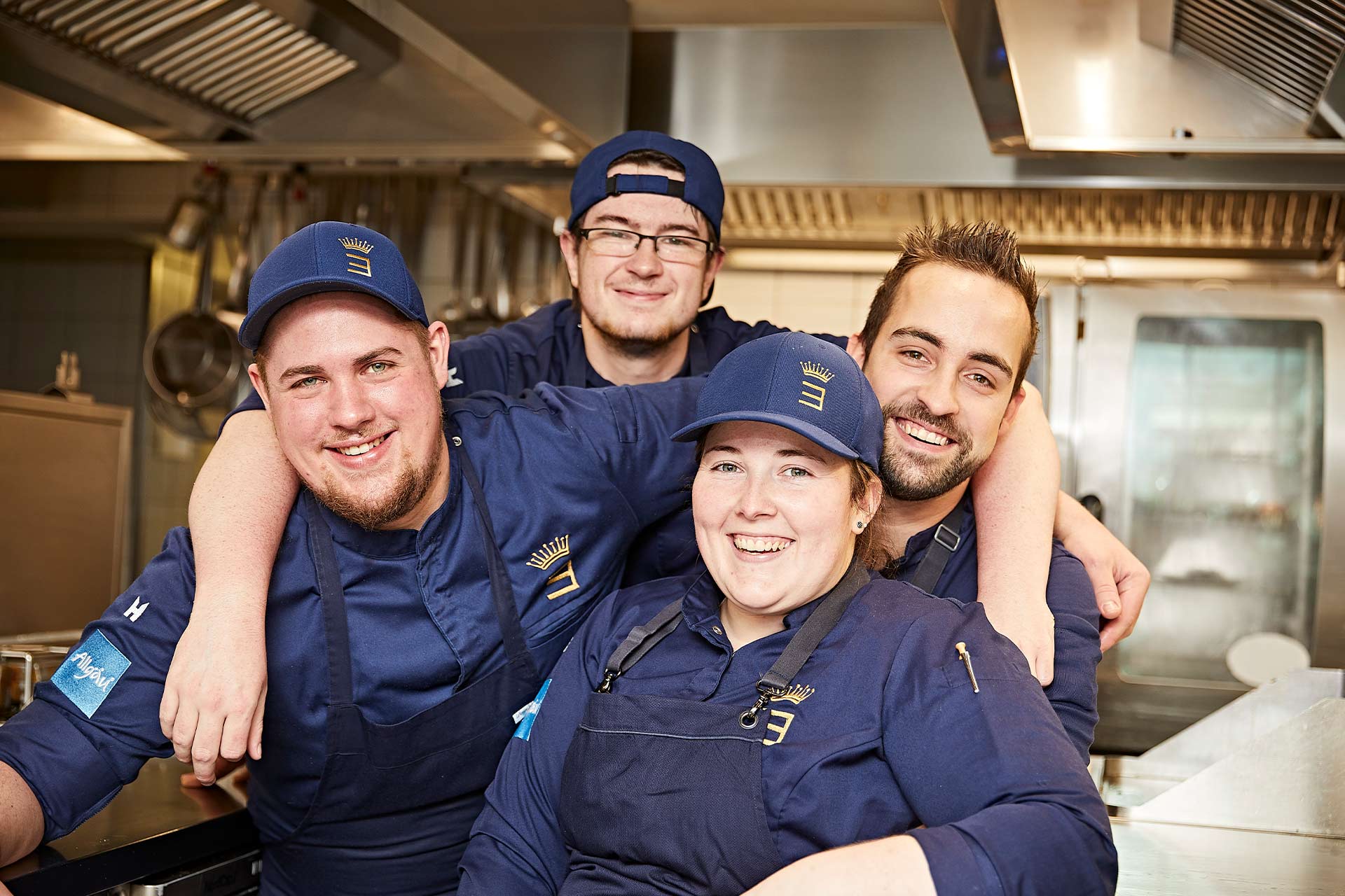 vier Köche stehen in der Küche und lachen herzlich in die Kamera