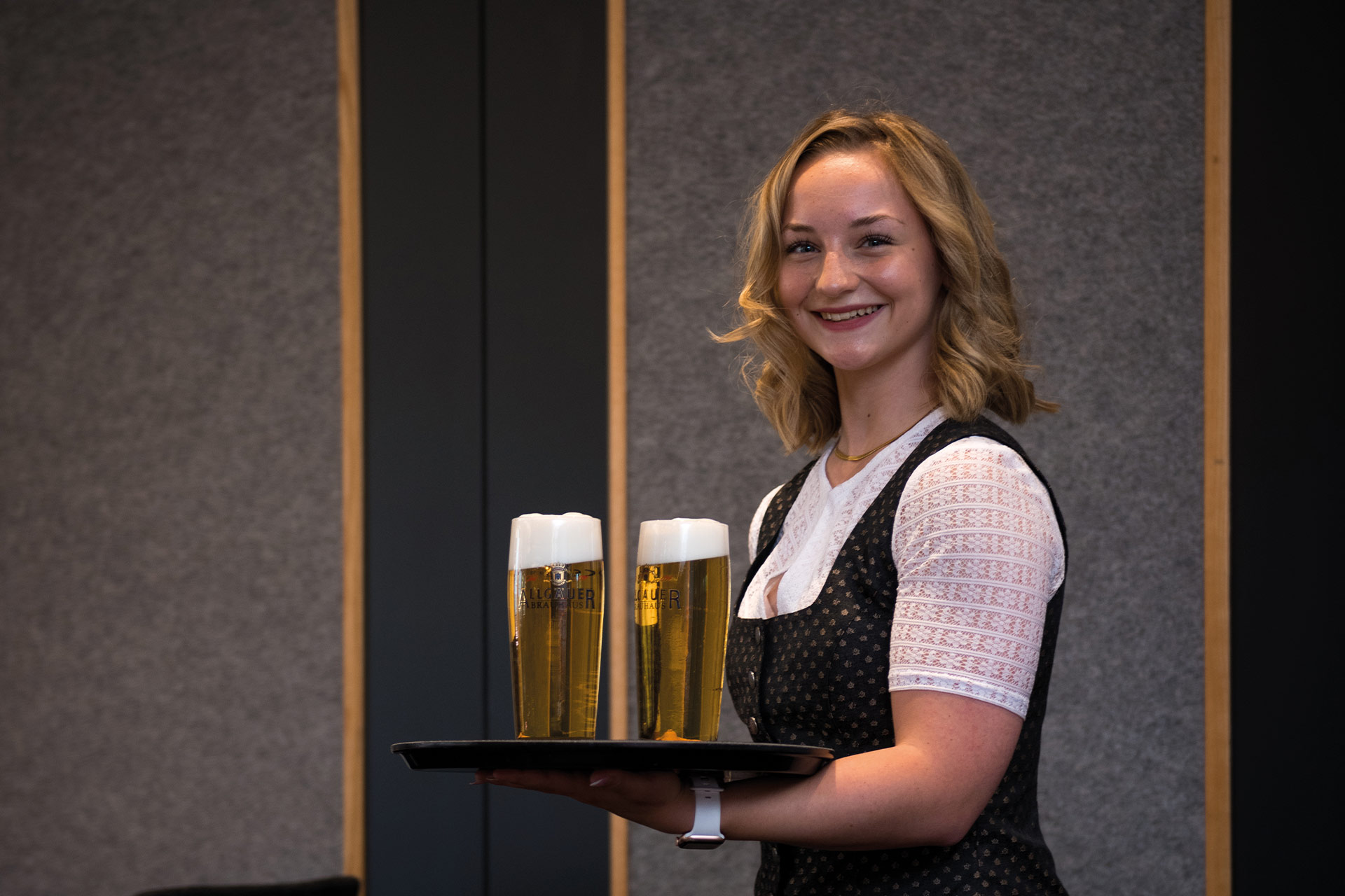 eine Junge Kellnerin läuft mit 2 Bier auf dem Tablett durch das Restaurant